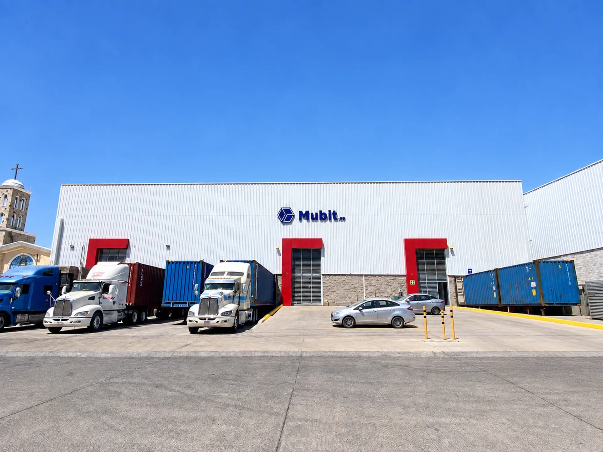 Fachada del almacén de Mubit en La Tijera con tráileres y contenedores en el andén